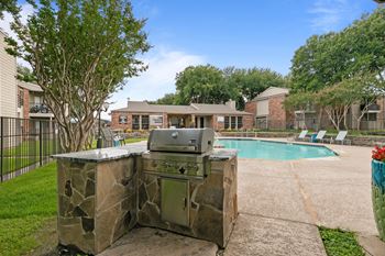 A stone BBQ grill is in the middle of a concrete patio.