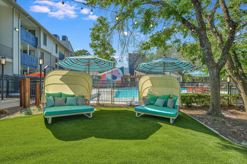 two lounge chairs with umbrellas in front of a pool at Peaks at Northwest Hills Apartments, Texas