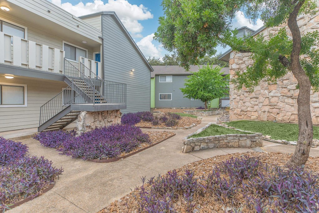 a patio with a stone wall and purple flowers in front of a building