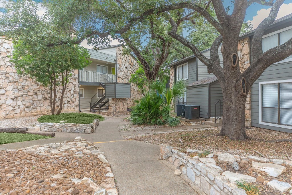 a walkway between two buildings with trees and rocks