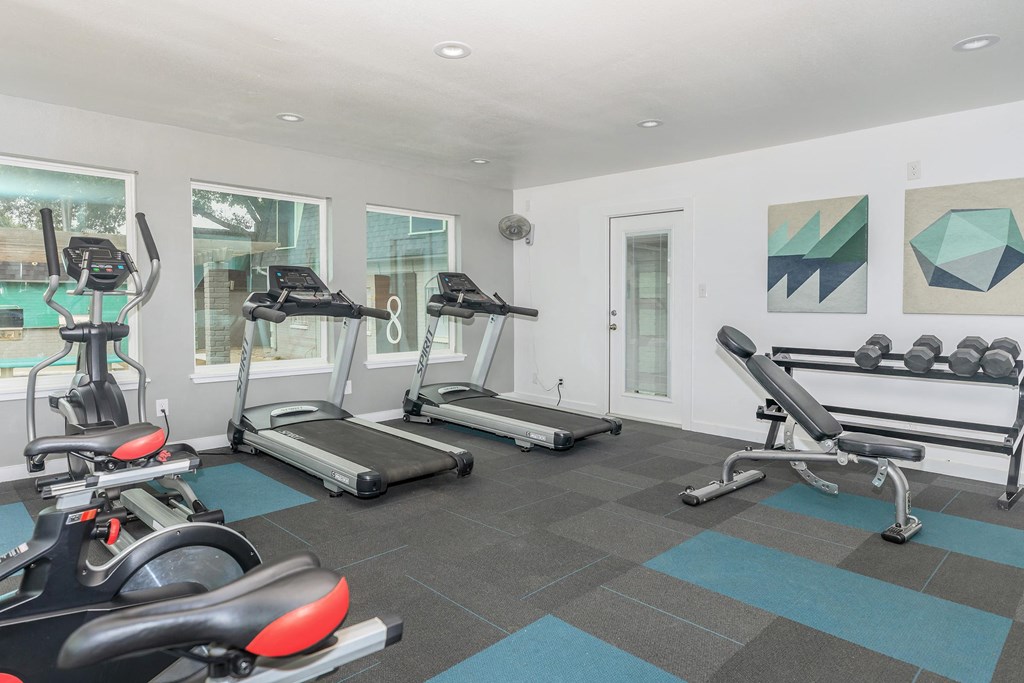 a gym with treadmills and other exercise equipment in a room with windows