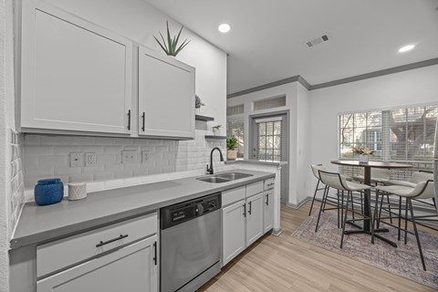 A modern kitchen with white cabinets and a wooden floor.