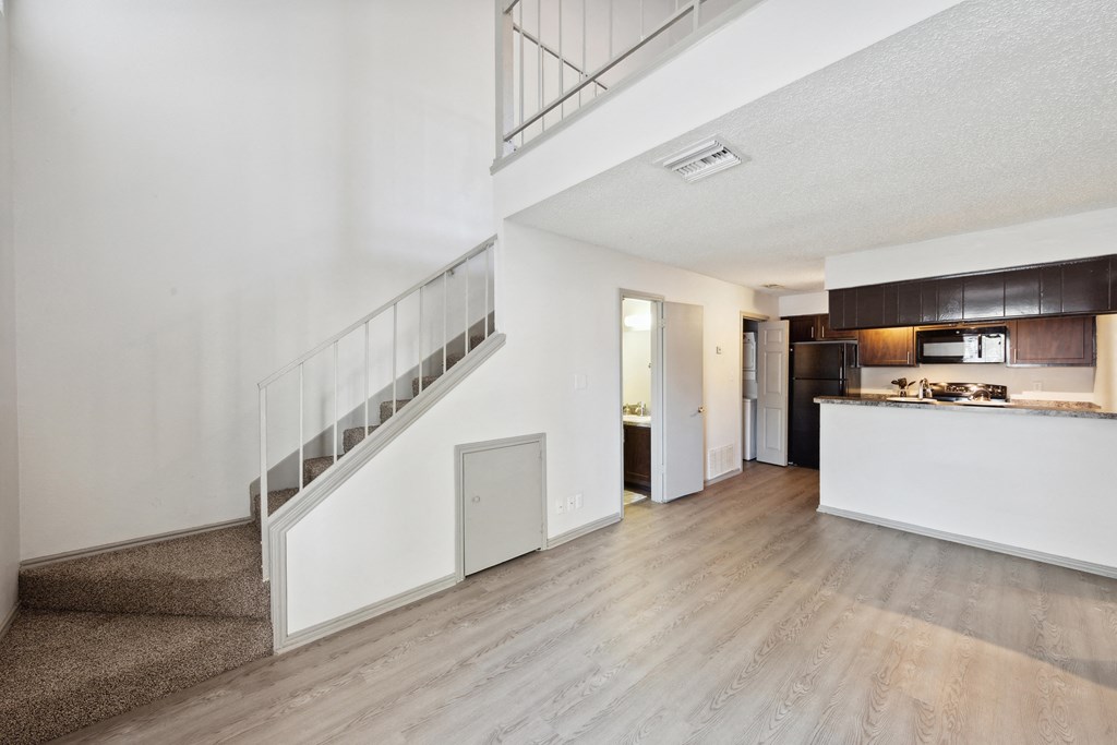 the living room and kitchen of an apartment with white walls and wood floors at Maxwell Townhomes, San Antonio