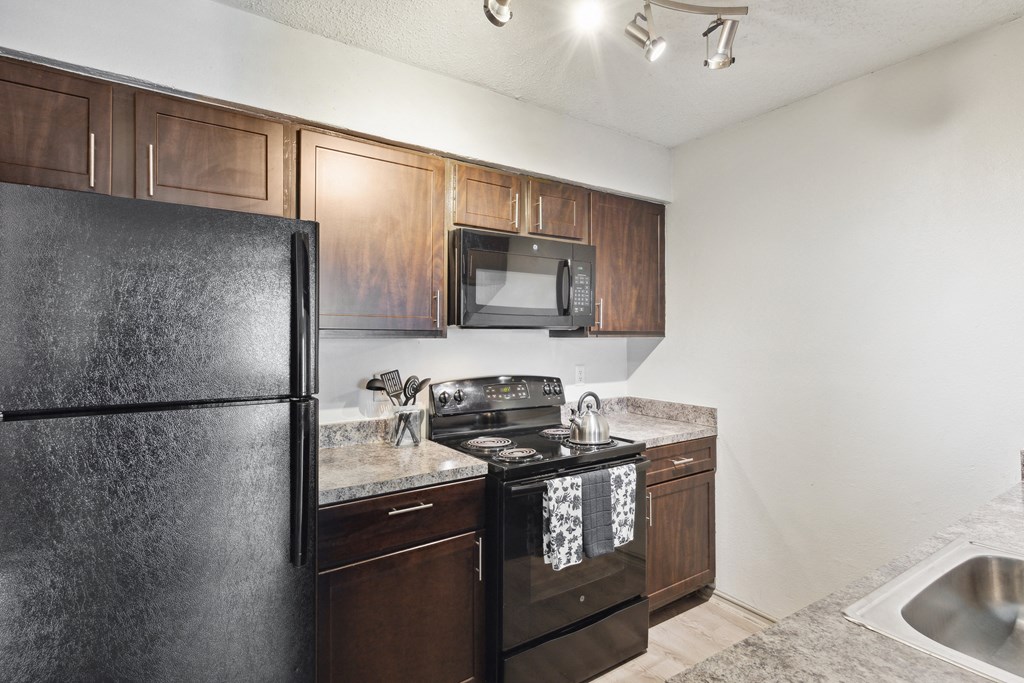 an apartment kitchen with black appliances and wood cabinets at Maxwell Townhomes, San Antonio, TX, 78230