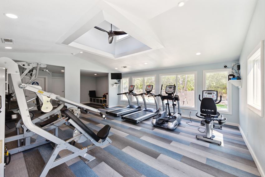 a gym with cardio machines and a ceiling fan