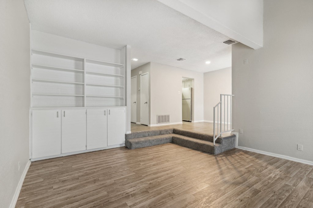 a living room with white walls and wood flooring and a staircase