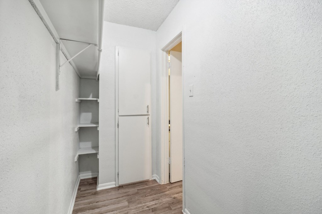 a walk-in closet with white walls and hardwood floors