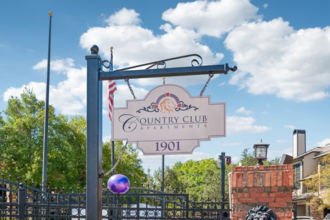 A sign for the Country Club Apartments is displayed in front of a gate.
