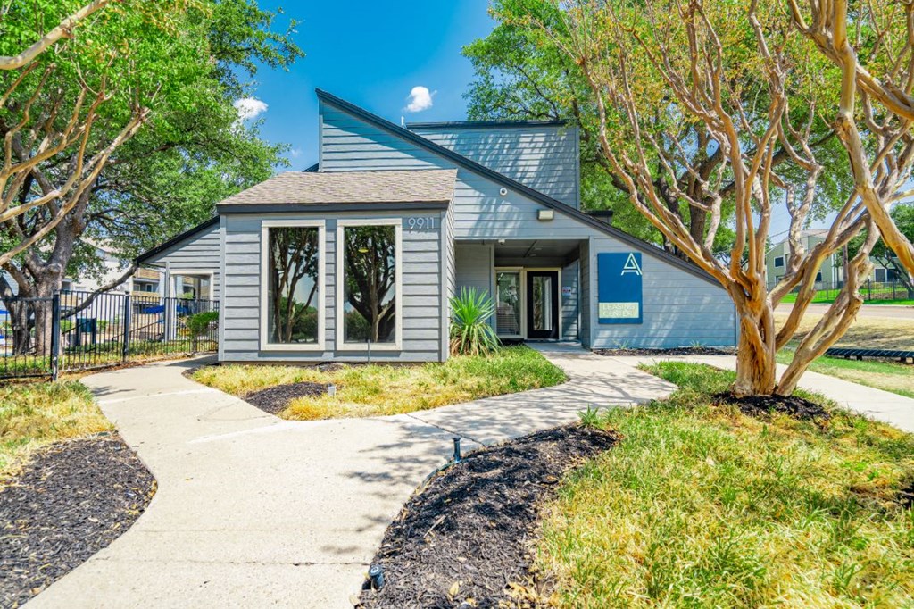 a gray building with a sidewalk and trees outside of it