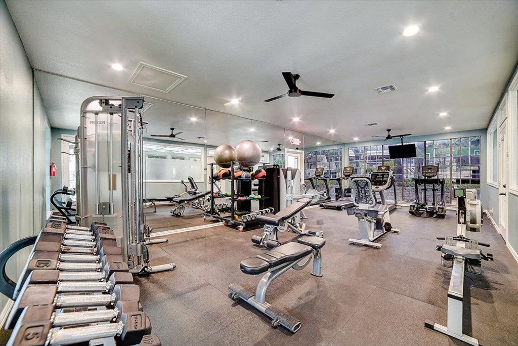 a gym with a lot of exercise equipment and a ceiling fan