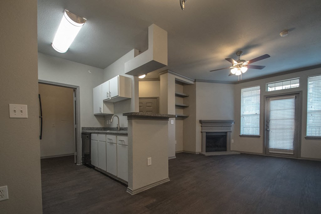 an empty living room with a kitchen and a ceiling fan