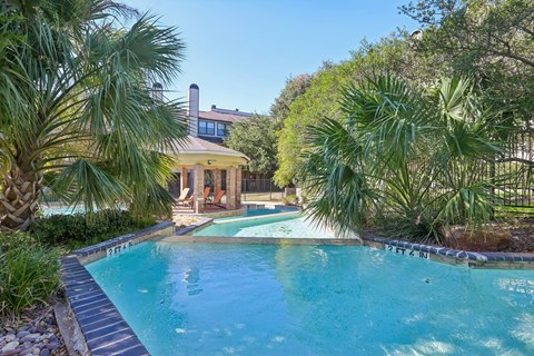 A pool surrounded by palm trees and a building in the background.