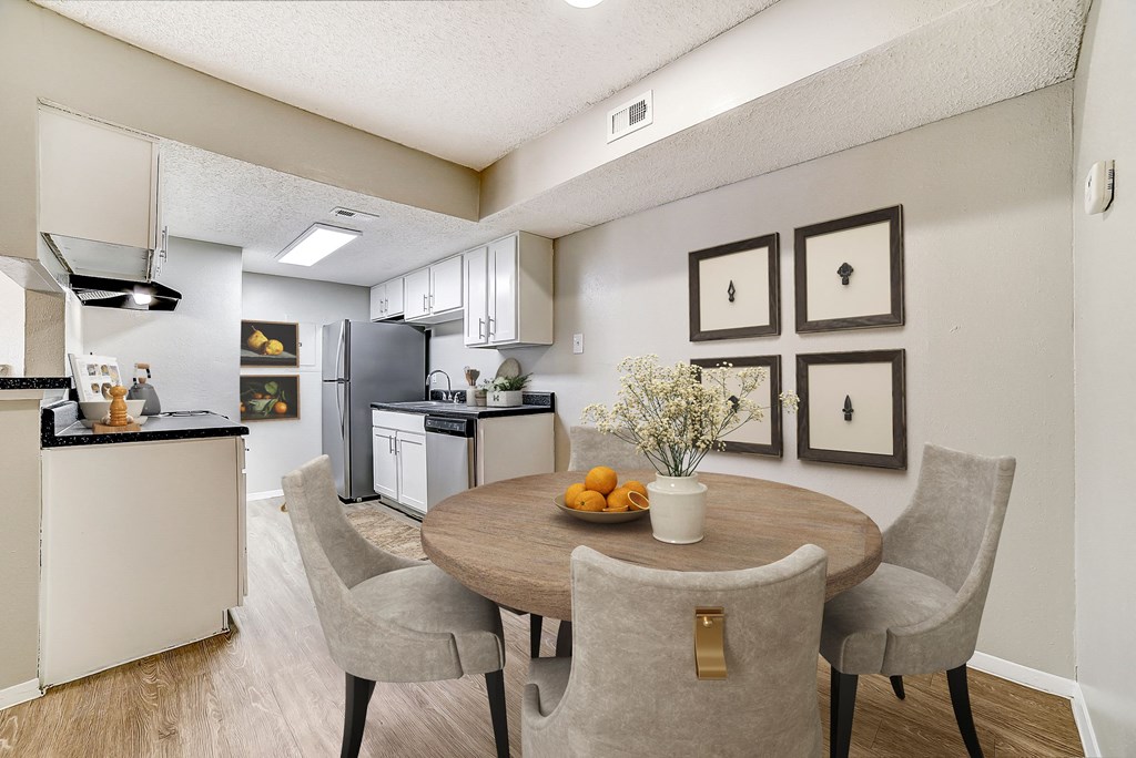 a dining area with a table and chairs and a kitchen in the background