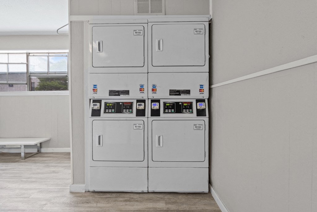 a row of white utility machines in a room with a bench