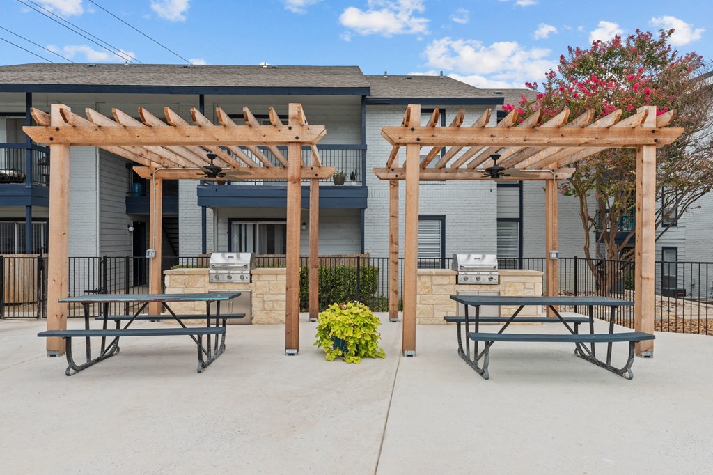 a picnic area with two picnic tables and a barbecue grill in front of a building