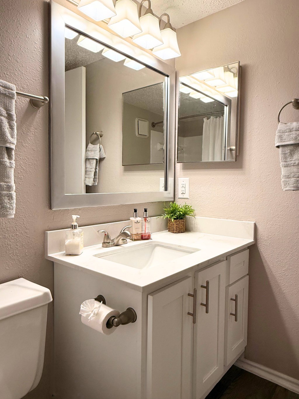A white bathroom with a toilet, sink, mirror and towel rack.