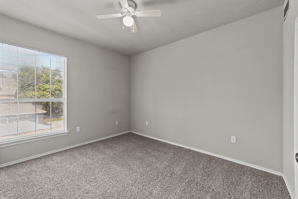 A room with a ceiling fan and a window overlooking a fence.