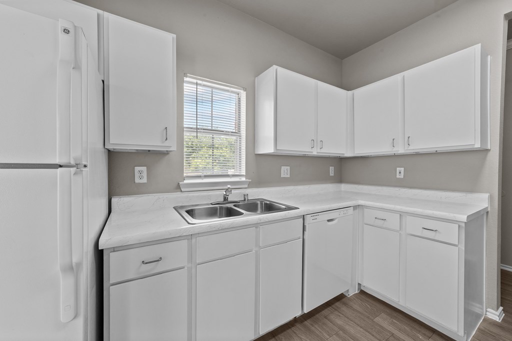 A white kitchen with a refrigerator, sink, and cabinets.