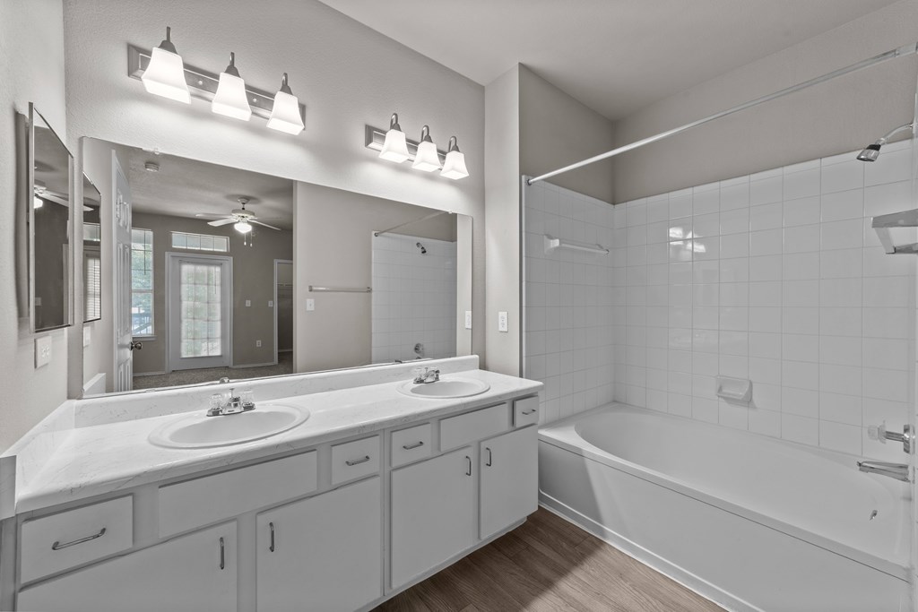 A bathroom with a white tub, sink, and mirror.