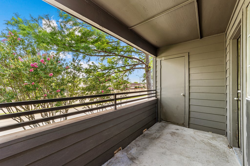 A balcony with a door and a railing with flowers in the background.