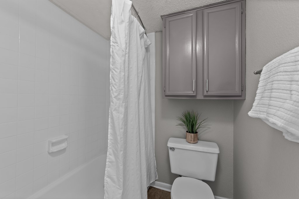 A white toilet sits in a bathroom next to a white shower curtain.