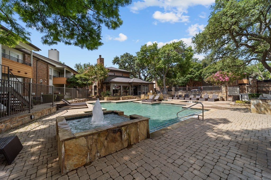 A pool with a fountain in the middle of a brick patio.