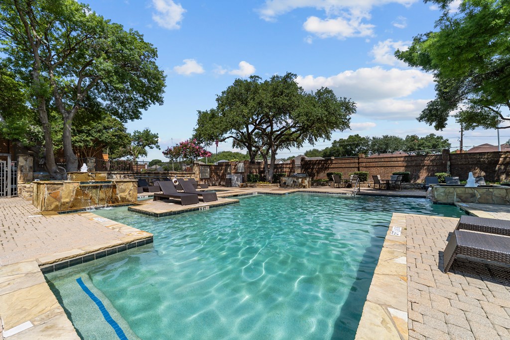 A large outdoor swimming pool surrounded by trees and lounge chairs.