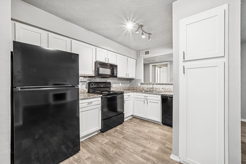 A black refrigerator stands in a kitchen with white cabinets and a black stove.