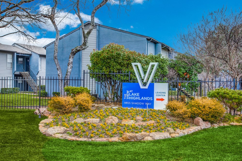 a round flower bed with yellow flowers in front of a blue building with a sign that says