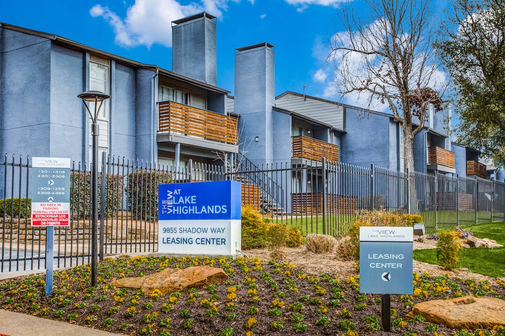 a blue and white sign is in the middle of a garden in front of an apartment building
