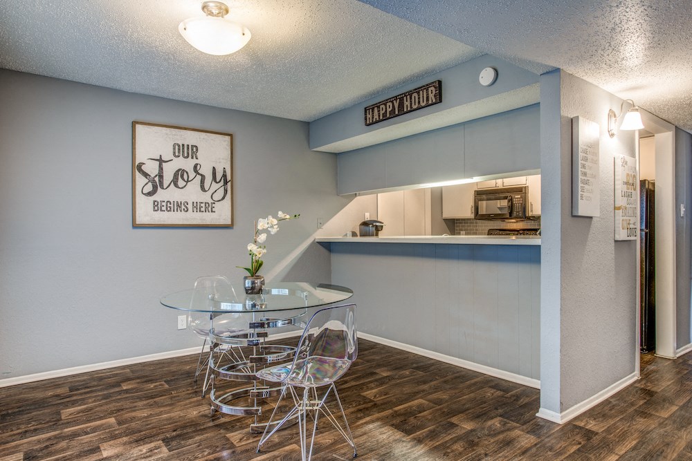 a dining area with a glass table and chairs and a kitchen in the background