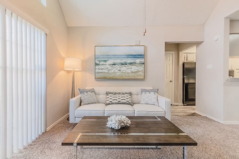 A living room with a white couch and a painting of a beach scene on the wall.