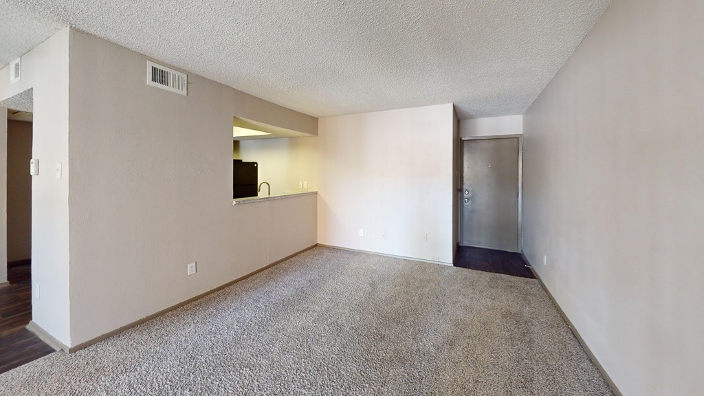 A spacious living room with a flat screen TV and a door leading to a kitchen.