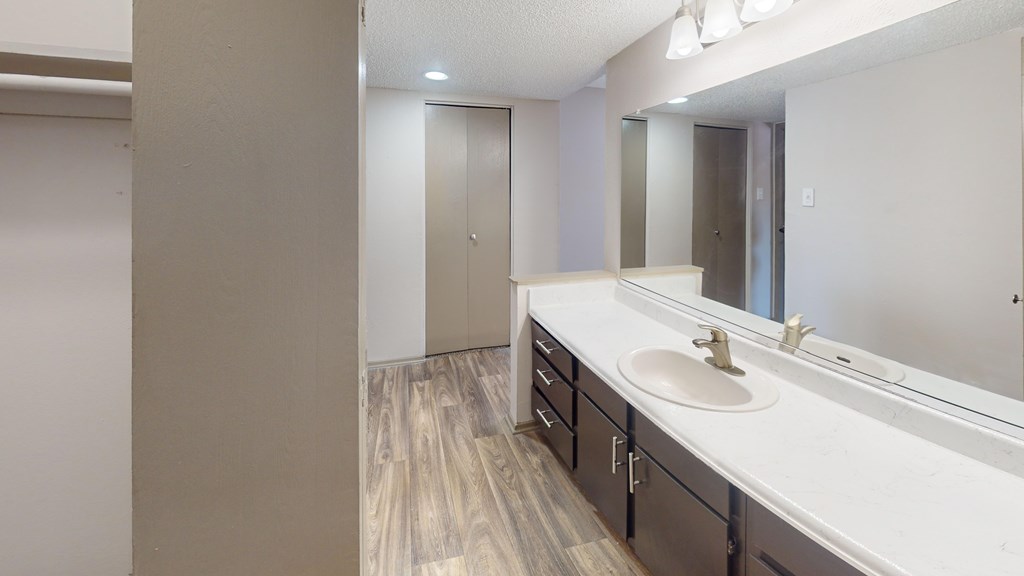 A bathroom with a sink, mirror, and wooden floors.