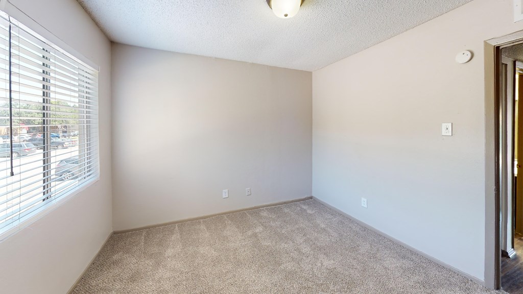 A room with a carpeted floor and a window with blinds.