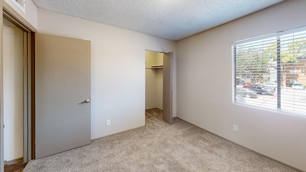 A room with a carpeted floor, a door, and a window with blinds.