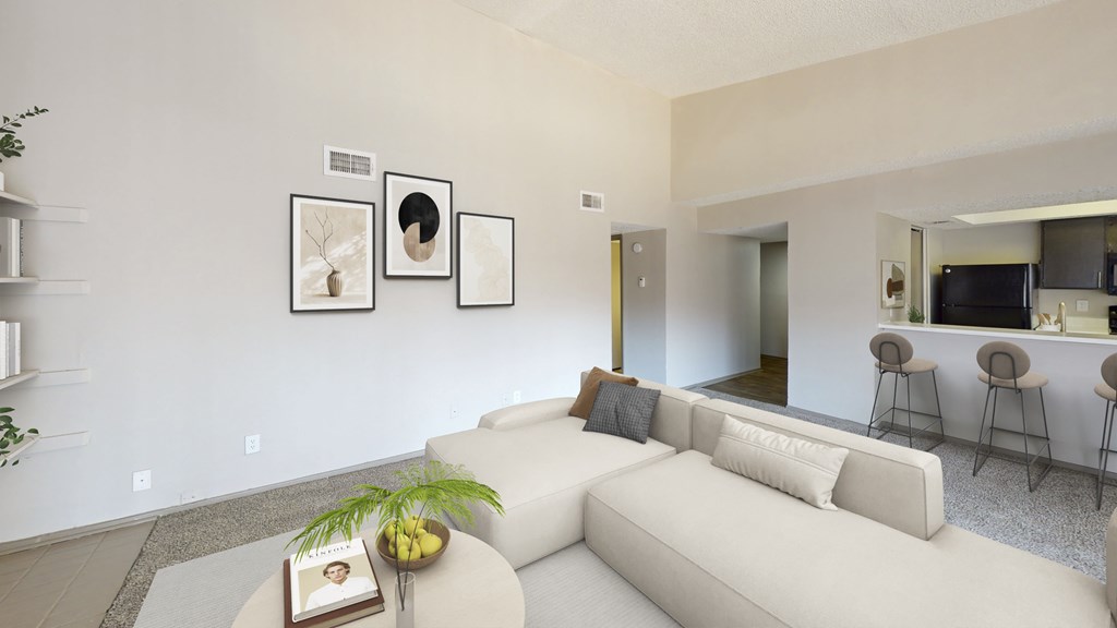 A living room with a white couch, a coffee table with a book and a plant on it, and a wall with three framed pictures.