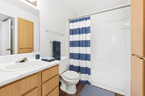A white sink with a wooden cabinet and a white toilet in a bathroom.