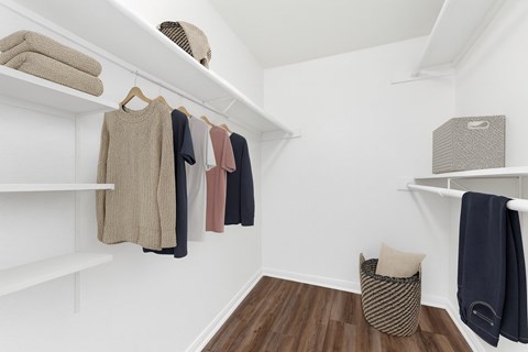 A white closet with clothes hanging and a basket on the floor.