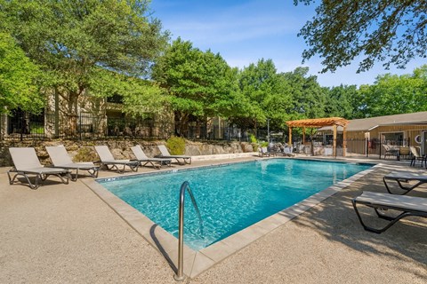 A pool surrounded by trees and lounge chairs.