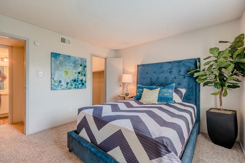 Bedroom with blue upholstered bed and geometric bedding at Cottages at Bedford Apartments, Bedford, 76021