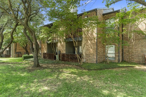 the front of a brick apartment building with grass and trees