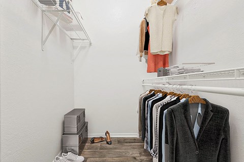 a walk in closet with a rack of sweaters and clothes hanging