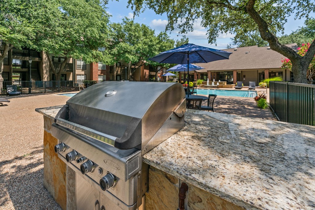 an outdoor kitchen with a grill and a swimming pool in the background