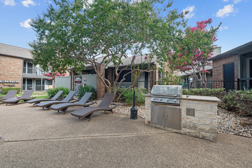 a barbecue and lounge chairs at legacy apartments in plano, tx