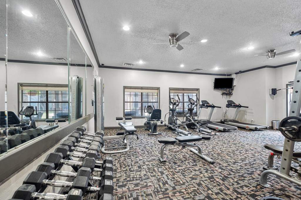 a spacious fitness center with cardio equipment and a flat screen tv