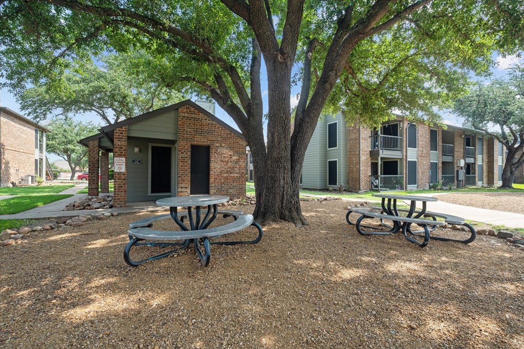 a picnic area with two tables and a tree in front of a brick building