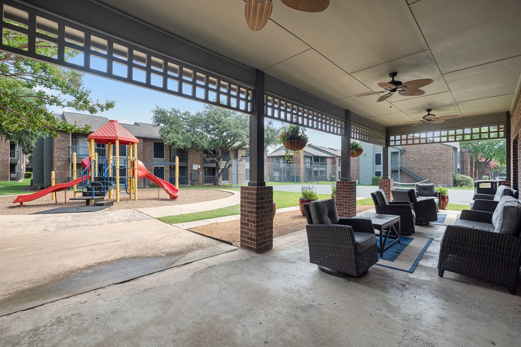 a covered patio with furniture and a playground in the background