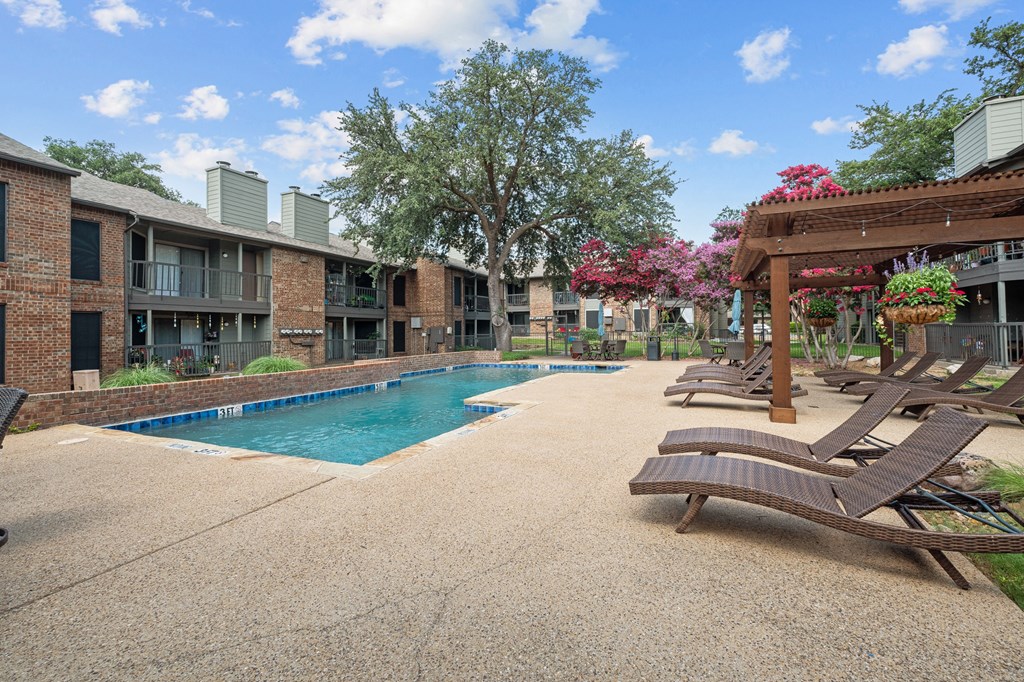 a swimming pool with chaise lounge chairs and a pergola in front of a brick