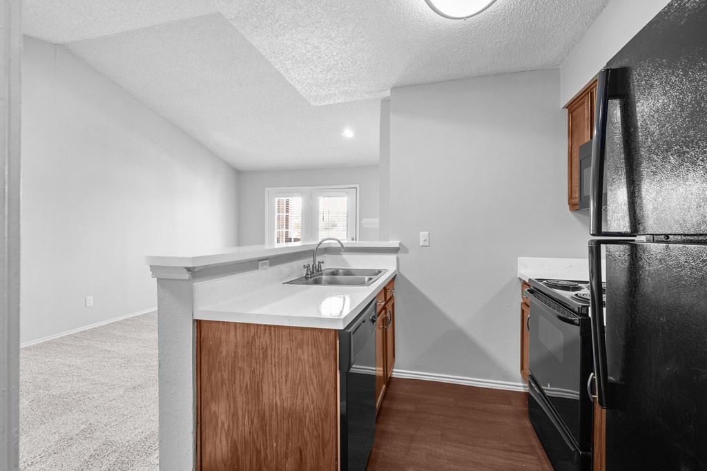A kitchen with a black refrigerator and wooden cabinets. at Preston Bend, Dallas